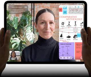 iPad Pro, front exterior, landscape orientation, space black color, rounded corners, black display bezel, hands holding left and right sides, display showing a FaceTime conversation being live translated, and an educational app showing a presentation of "Comparative Mythology" with text, diagrams, and handwritten notes