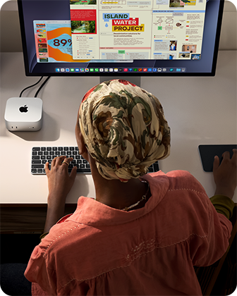 A person typing at a desk with a Mac mini, Studio Display connected, Magic Keyboard, Magic Trackpad, various items