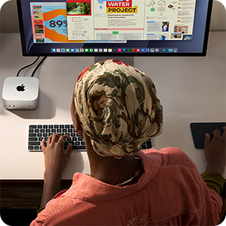 A person typing at a desk with a Mac mini, Studio Display connected, Magic Keyboard, Magic Trackpad, various items