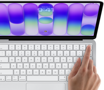 MacBook Neo, silver color, showing login screen, person's finger on Touch ID sensor in top-right corner of keyboard