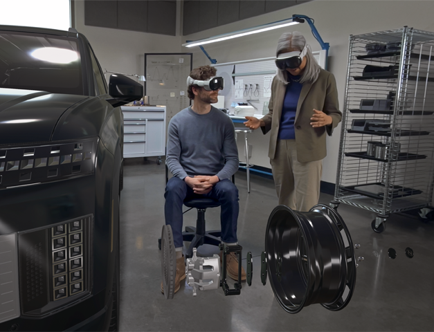 Two designers wearing Apple Vision Pro interact with a 3D projection of internal components of a car's wheel inside an automative design facility
