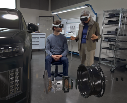 Two designers wearing Apple Vision Pro interact with a 3D projection of internal components of a car's wheel inside an automative design facility