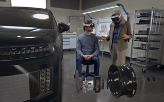 Two designers wearing Apple Vision Pro interact with a 3D projection of internal components of a car's wheel inside an automative design facility