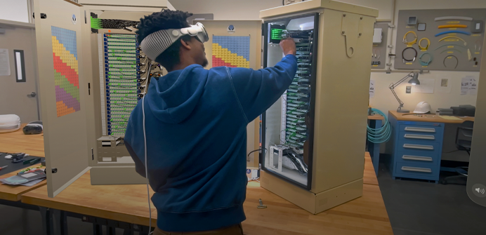 A technician stands at a table and assembles an electrical server tower while wearing Apple Vision Pro and referencing a 3D projection of the tower
