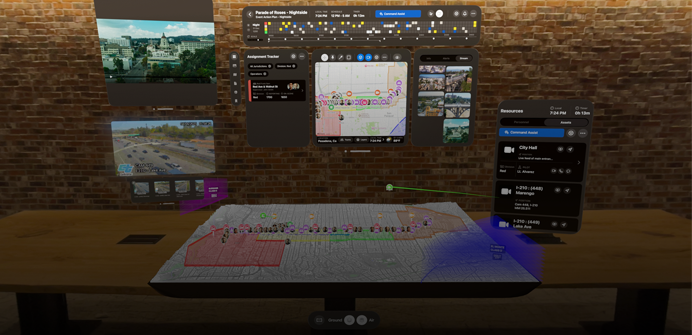 From the view of someone using Apple Vision Pro, a 3D projection of dashboards shows camera feeds, team assignments, and a map of a parade route, in front of a brick wall inside an office