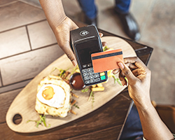 A restaurant waiter using a mobile POS device to accept a credit card payment at the customer's table.