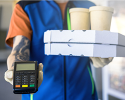 A restaurant employee with a mobile POS device carries a customer's order to their car for contactless curbside pickup.